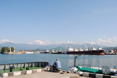 Yaşlı bir adam yatların arasında iskelede balık tutuyor..