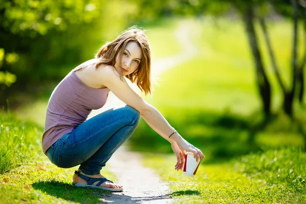 Young happy Caucasian blonde woman with coffee beverage sitting in park. — Stock Photo, Image