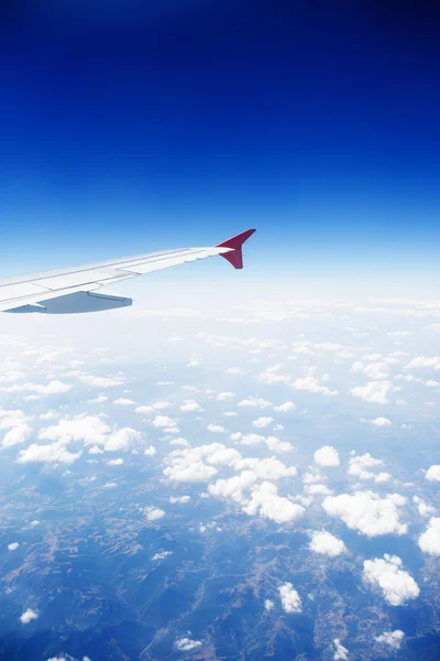 Wing of an airplane flying above the clouds and mountains.