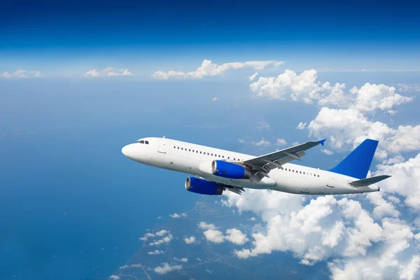 Large passenger airplane flying over clouds in blue sky.