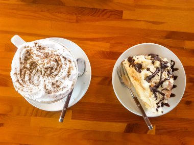 Kapuçino kahvesi. Bir fincan cappuccino, latte, tahtadan bir masanın üzerinde duruyor. Yanında da tatlı bir dilim pasta, kontun harabeleri.