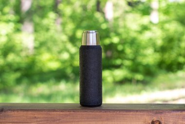 Çay ya da kahve demlenmiş siyah bir termos kopyalanmış bir tahta üzerinde duruyor. Sıcak içecekli termos.