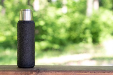 Çay ya da kahve demlenmiş siyah bir termos kopyalanmış bir tahta üzerinde duruyor. Sıcak içecekli termos.