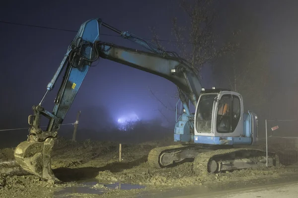 Blue excavator digger working at night on the stree