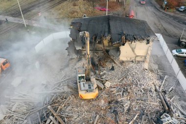 Sarı kazıcı binayı yok ediyor. Ağır iş makineleri bir tuğla binayı yıkıyor. Binanın yıkılması. Yıkım inşaat işi hava aracı fotoğraf görüntüsü