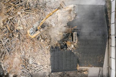 Sarı kazıcı binayı yok ediyor. Ağır iş makineleri bir tuğla binayı yıkıyor. Binanın yıkılması. Yıkım inşaat işi hava aracı fotoğraf görüntüsü