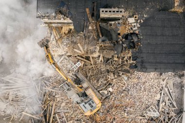 Sarı kazıcı binayı yok ediyor. Ağır iş makineleri bir tuğla binayı yıkıyor. Binanın yıkılması. Yıkım inşaat işi hava aracı fotoğraf görüntüsü