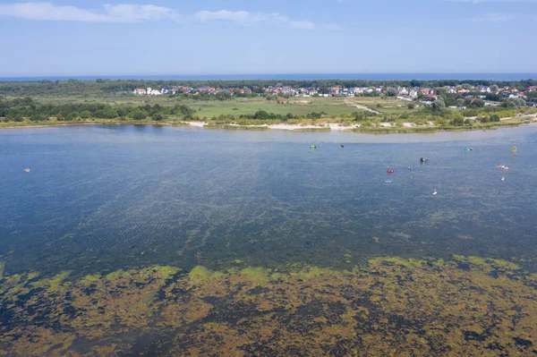 People swim in the sea on a kiteboard or kitesurfing. Summer sport learning how to kitesurf. Kite surfing on Puck bay in Jastarnia, Poland, Europe aerial drone photo view