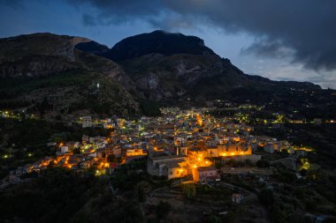 Collesano 'nun hava aracı gece görüşü. Sicilya' nın Sicilya bölgesindeki Madonie Dağları 'nda Basilica San Pietro kilisesi ve aydınlık taş sokaklar ile birlikte alacakaranlıkta tarihi bir Sicilya dağ kasabası..