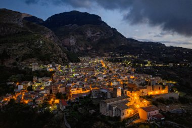 Collesano 'nun hava aracı gece görüşü. Sicilya' nın Sicilya bölgesindeki Madonie Dağları 'nda Basilica San Pietro kilisesi ve aydınlık taş sokaklar ile birlikte alacakaranlıkta tarihi bir Sicilya dağ kasabası..