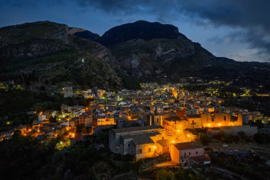 Collesano 'nun hava aracı gece görüşü. Sicilya' nın Sicilya bölgesindeki Madonie Dağları 'nda Basilica San Pietro kilisesi ve aydınlık taş sokaklar ile birlikte alacakaranlıkta tarihi bir Sicilya dağ kasabası..