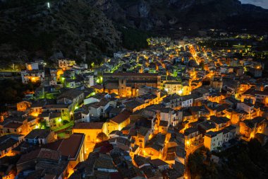 Collesano 'nun hava aracı gece görüşü. Sicilya' nın Sicilya bölgesindeki Madonie Dağları 'nda Basilica San Pietro kilisesi ve aydınlık taş sokaklar ile birlikte alacakaranlıkta tarihi bir Sicilya dağ kasabası..