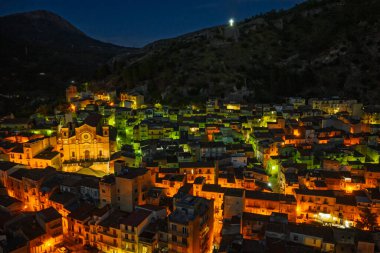 Collesano 'nun hava aracı gece görüşü. Sicilya' nın Sicilya bölgesindeki Madonie Dağları 'nda Basilica San Pietro kilisesi ve aydınlık taş sokaklar ile birlikte alacakaranlıkta tarihi bir Sicilya dağ kasabası..