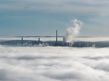 Güneşli bir günde, yoğun sis ve bulutların üzerine buhar yayan endüstriyel bacaların hava aracı görüntüsü, enerji santrali ve fabrika manzarası. Güneşli bir günde bulutların üzerindeki panorama. Bulut fabrikası.