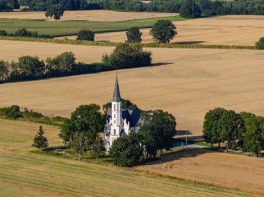 Polonya 'nın Sidzina yakınlarındaki tarlalarda, altın tahıl tarlaları ve açık kırsal alanlarla çevrili neo gotik kilisenin insansız hava aracı fotoğrafı. Huzurlu kırsal bir manzara..