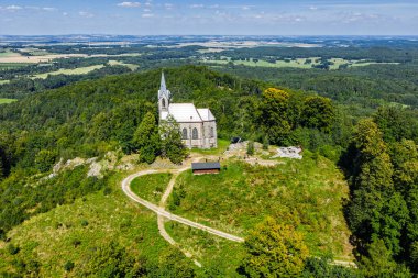 Çek Cumhuriyeti 'nin Bozi Hora tepesindeki tarihi kilisesinin, geleneksel çatılarının, yeşilliğin çevresindeki Zulova kasabasının insansız hava aracı görüntüsü ve gün ışığında yakalanan huzurlu kasaba düzeni..