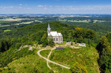 Çek Cumhuriyeti 'nin Bozi Hora tepesindeki tarihi kilisesinin, geleneksel çatılarının, yeşilliğin çevresindeki Zulova kasabasının insansız hava aracı görüntüsü ve gün ışığında yakalanan huzurlu kasaba düzeni..