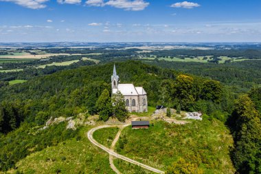 Çek Cumhuriyeti 'nin Bozi Hora tepesindeki tarihi kilisesinin, geleneksel çatılarının, yeşilliğin çevresindeki Zulova kasabasının insansız hava aracı görüntüsü ve gün ışığında yakalanan huzurlu kasaba düzeni..