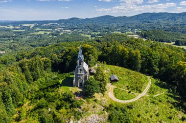 Çek Cumhuriyeti 'nin Bozi Hora tepesindeki tarihi kilisesinin, geleneksel çatılarının, yeşilliğin çevresindeki Zulova kasabasının insansız hava aracı görüntüsü ve gün ışığında yakalanan huzurlu kasaba düzeni..