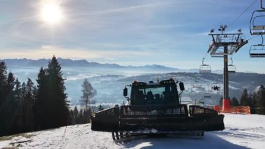 Zakopane yakınlarındaki kayak pistini hazırlayan kar temizleme makinesi ve arka planda Tatra Dağları. Piste bakımını, dağlık araziyi ve güneşli bir günü gösteren kış oteli sahnesi.
