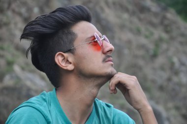 Güneş gözlüğü takan genç bir adamın yakından çekilmiş fotoğrafı, dışarıda oturuyor ve eli çenesinde yukarı bakıyor, insanlar şöyle düşünüyor: