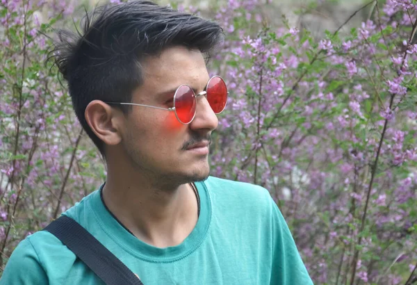 Front view of a good looking Indian guy wearing sunglass while standing outdoor and looking sideways, People in nature - Stock Photo