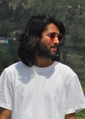 Yakışıklı, uzun saçlı, güneş gözlüğü takan, yan bakan, dışarıda beyaz tişörtlü, sakallı, yakışıklı bir adamın portresi.