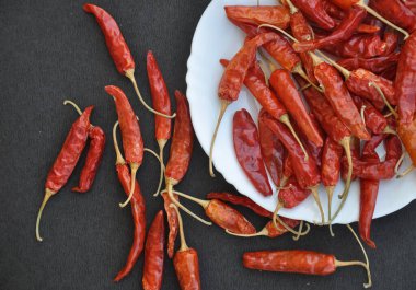 Beyaz tabakta kırmızı biber yığınının kabataslak desenli siyah masaya yayılmış görüntüsü. 