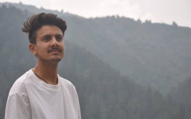 Tepede üzerinde beyaz t-shirt olan genç bir adamın fotoğrafı.