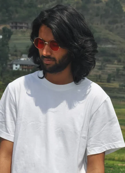 一个英俊的印度长发小伙子头戴墨镜 低头看 一个英俊的大胡子小伙子站在外面 身穿白色T恤的画像 — 图库照片