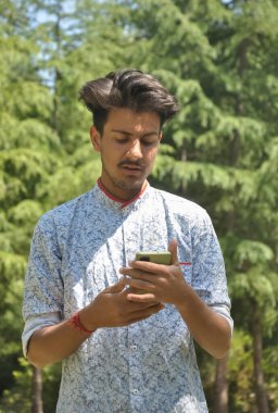 Dışarıda cep telefonu kullanan Hintli yakışıklı bir gencin portresi.