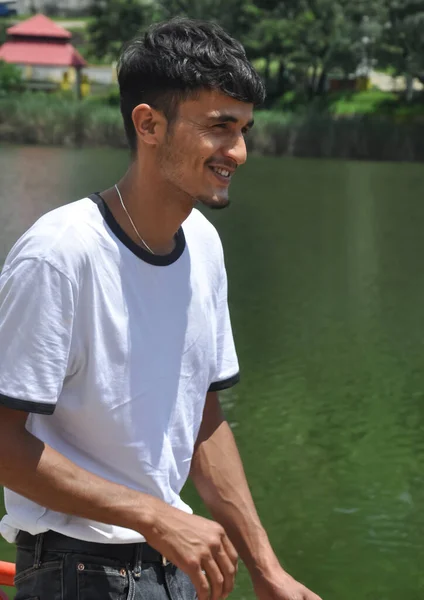 一个穿着白色T恤站在湖边微笑的印度年轻人的画像 — 图库照片