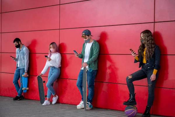 Young people wearing face safety masks using smart mobile phones while keeping social distance during coronavirus time - Technology and covid-19 spread prevention concept