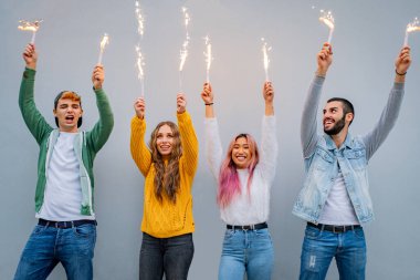Bir grup çoklu etnik arkadaş maytaplarla oynuyorlar ellerinde maytaplarla dans eden insanlar bir partide Bengal lambası tutan gençlerin görüntülerini çekiyorlar.