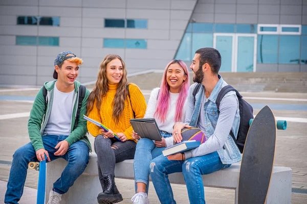 多民族学生冗談と一緒に大学で屋外のベンチに座って話 本やタブレットで勉強幸せな若い十代の若者のグループ — ストック写真