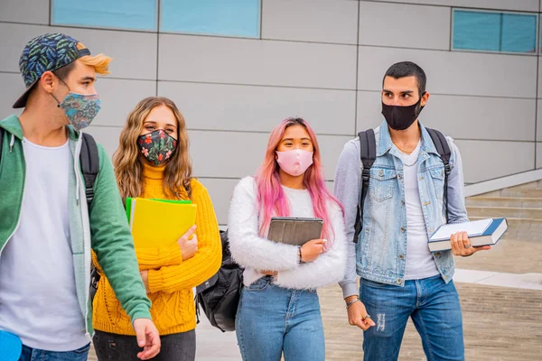 Üniversite çıkışında maskeli çok ırklı öğrenciler - bir grup genç, salgın hastalıktan korunma maskesi takmış, tartışıyorlar ve sokakta yürüyorlar.