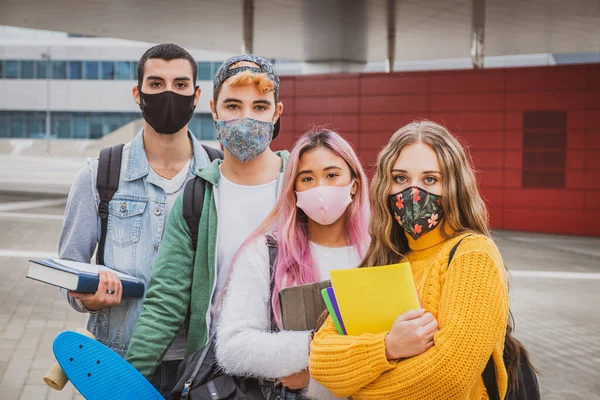 Eğitim, sağlık ve salgın konsepti - Gezen ve konuşan sırt çantalı bir grup üniversite öğrencisi, virüs hastalığından korunmak için yüz koruyucu maskeler takıyor