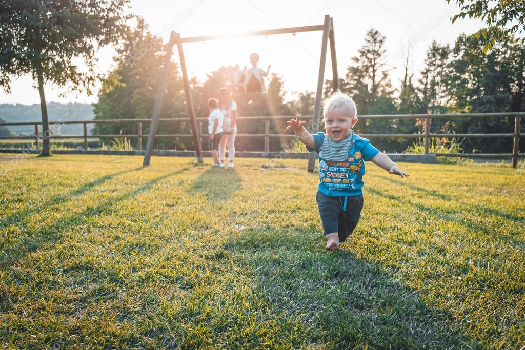 One year old boy running barefoot in the playground on a beautiful spring day - Cute little boy taking his first steps at sunset - Learn to walk concept. Goes alone