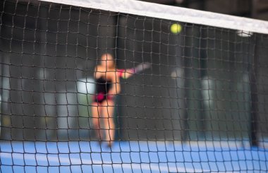 Kadın kapalı tenis kortunda padel oynuyor.