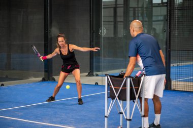 Öğrencisi Padel 'den kadınlara ders verirken gözlemci - Antrenör, genç kıza kapalı tenis kortunda nasıl Padel oynanacağını öğretiyor