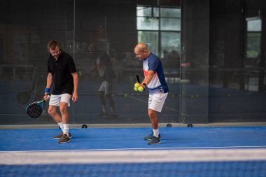 Öğrencisi Padel 'in erkek öğrencisine ders verirken gözlemci çocuğa kapalı tenis kortunda nasıl Padel oynanacağını öğretiyor.