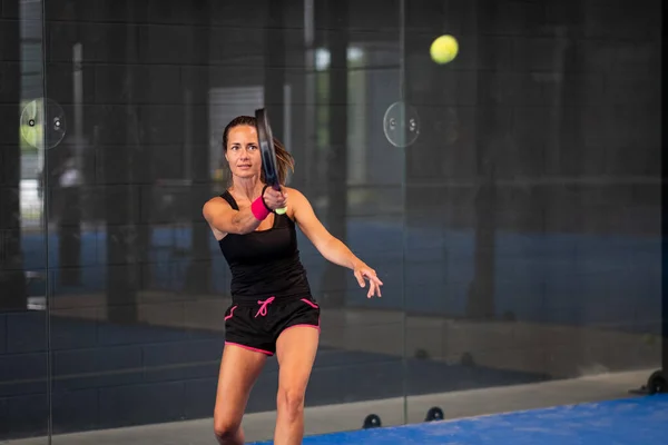 Kapalı alanda padel oynayan bir kadın genç sporcu kadın raketle topa vuruyor.
