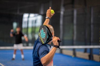 Öğrencisi Padel 'in erkek öğrencisine ders verirken gözlemci çocuğa kapalı tenis kortunda nasıl Padel oynanacağını öğretiyor.