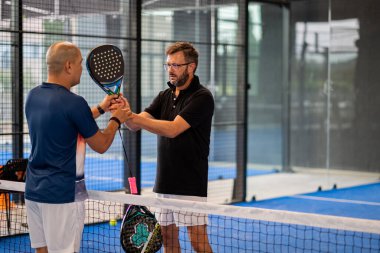 Öğrencisi Padel 'in erkek öğrencisine ders verirken gözlemci çocuğa kapalı tenis kortunda nasıl Padel oynanacağını öğretiyor.
