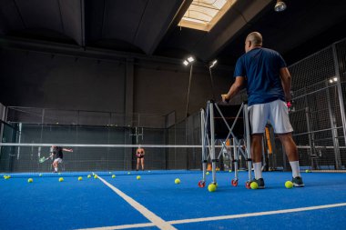 Öğrencileri Padel sınıfını erkek ve kadına öğretirken gözlemci - Antrenör kapalı tenis kortunda nasıl padel oynanacağını öğretiyor