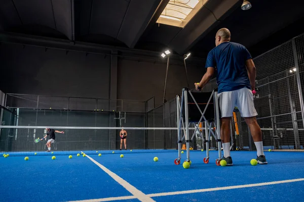 Öğrencileri Padel sınıfını erkek ve kadına öğretirken gözlemci - Antrenör kapalı tenis kortunda nasıl padel oynanacağını öğretiyor