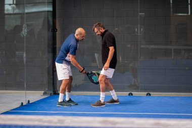 Öğrencisi Padel 'in erkek öğrencisine ders verirken gözlemci çocuğa kapalı tenis kortunda nasıl Padel oynanacağını öğretiyor.
