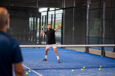 Öğrencisi Padel 'in erkek öğrencisine ders verirken gözlemci çocuğa kapalı tenis kortunda nasıl Padel oynanacağını öğretiyor.