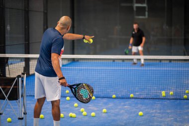 Öğrencisi Padel 'in erkek öğrencisine ders verirken gözlemci çocuğa kapalı tenis kortunda nasıl Padel oynanacağını öğretiyor.