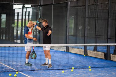 Öğrencisi Padel 'in erkek öğrencisine ders verirken gözlemci çocuğa kapalı tenis kortunda nasıl Padel oynanacağını öğretiyor.